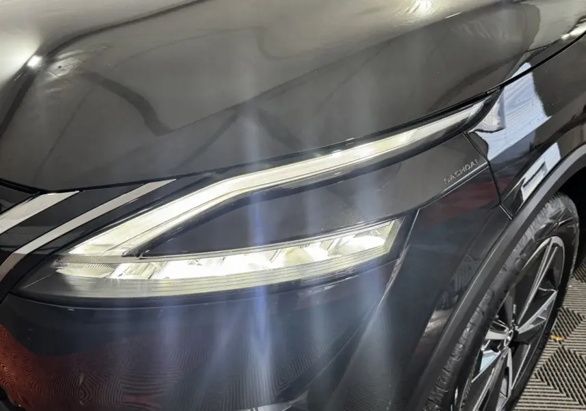 Gros plan sur le phare avant droit du Nissan Qashqai e-Power noir, soulignant le design LED et la jante alliage visible.