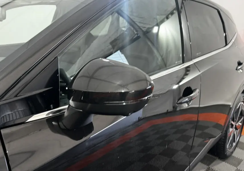Vue rapprochée du rétroviseur côté gauche d’un Nissan Qashqai e-Power noir brillant avec porte et jante partiellement visibles.