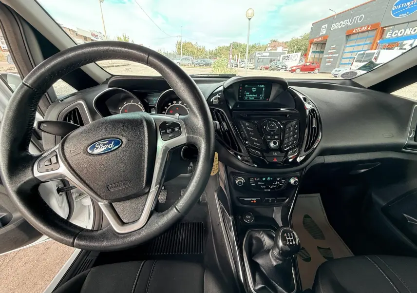 Vue intérieure du poste de conduite d'une Ford B-MAX blanche de 2014, volant et levier de vitesses manuelle visibles.