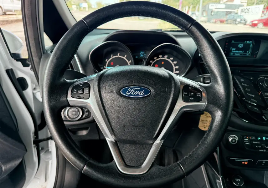 Vue rapprochée du volant en cuir noir d'une Ford B-MAX blanche de 2014, avec tableau de bord et commandes visibles.