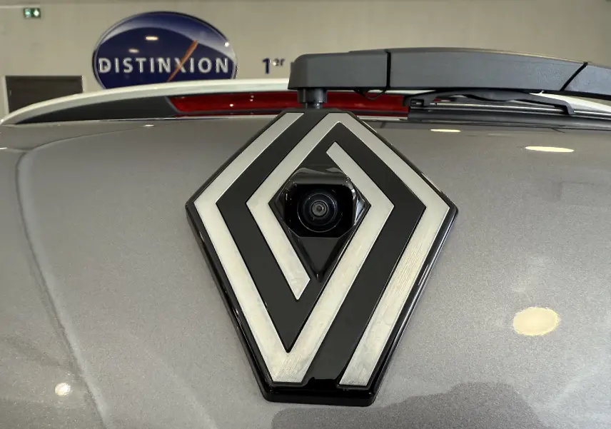 Gros plan sur le logo Renault gris métallisé avec caméra intégrée, sur le coffre arrière d’un Captur gris Cassiopée.