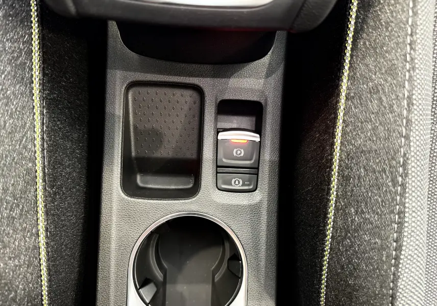 Gros plan sur la console centrale du Renault Captur 2025, montrant le porte-gobelet et les boutons de frein à main électrique et start/stop.
