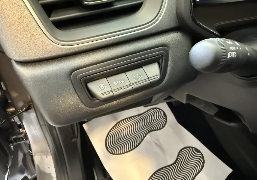 Vue intérieure côté gauche du tableau de bord du Renault Captur 2025, boutons de commandes E-SAVE et réglage phares visibles.