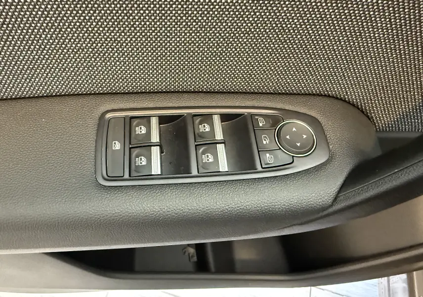 Gros plan sur les commandes de lève-vitres et rétroviseurs côté gauche de la porte d’un Renault Captur gris cassiopée 2025.