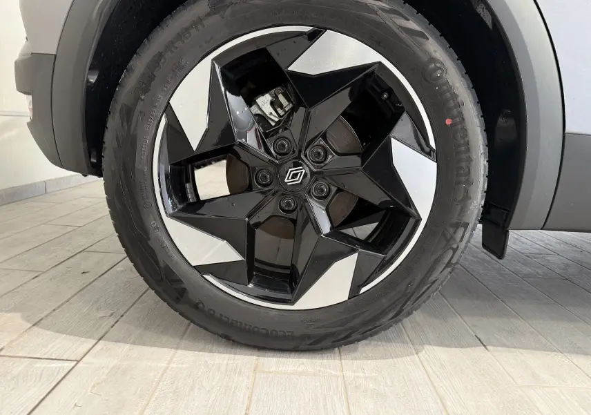 Gros plan sur la roue avant droite du Renault Captur gris Cassiopée, mettant en valeur la jante noire et argentée au design géométrique.