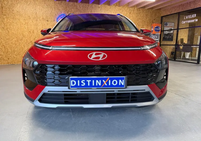 Vue frontale d'un Hyundai Bayon rouge avec calandre noir laqué et plaque Distinxion en intérieur d'atelier.