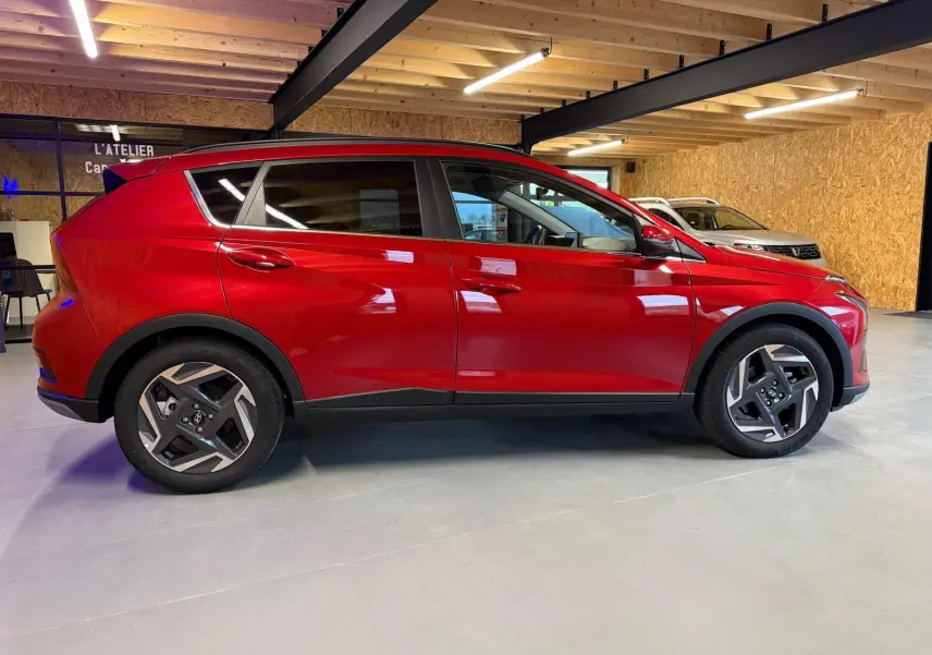 Profil droit d'un Hyundai Bayon rouge 2025 avec jantes alu 17'' et calandre noir laqué en intérieur d'atelier.