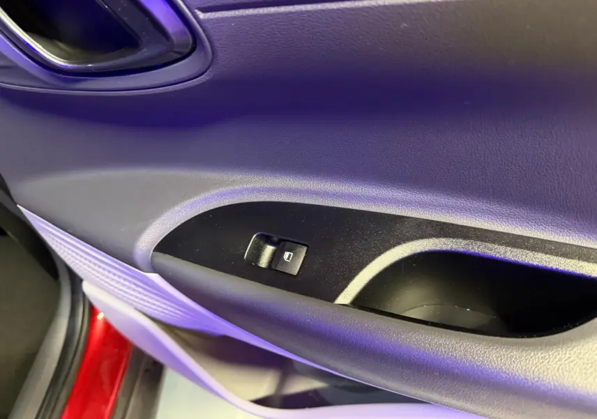 Gros plan sur la commande de lève-vitre côté conducteur d'une Hyundai Bayon rouge, intérieur noir.