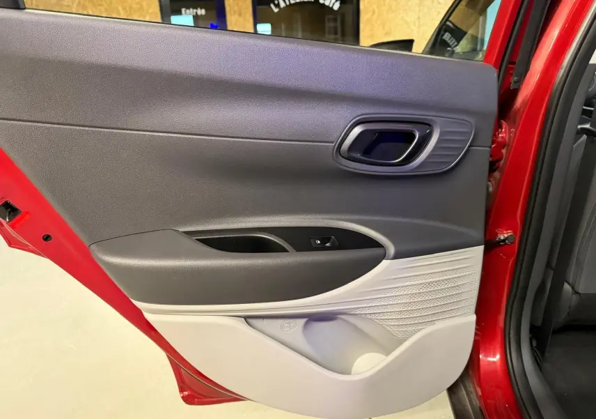 Porte arrière côté gauche ouverte d'une Hyundai Bayon rouge, intérieur bi-ton noir et gris clair avec poignée chromée.