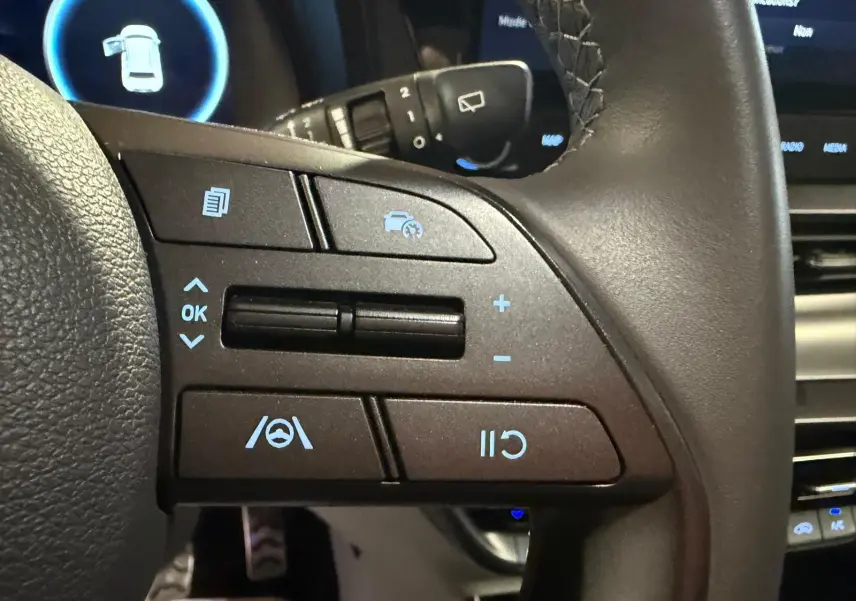 Gros plan sur les commandes multifonctions du volant cuir noir du Hyundai Bayon 2025, avec affichage numérique en arrière-plan.