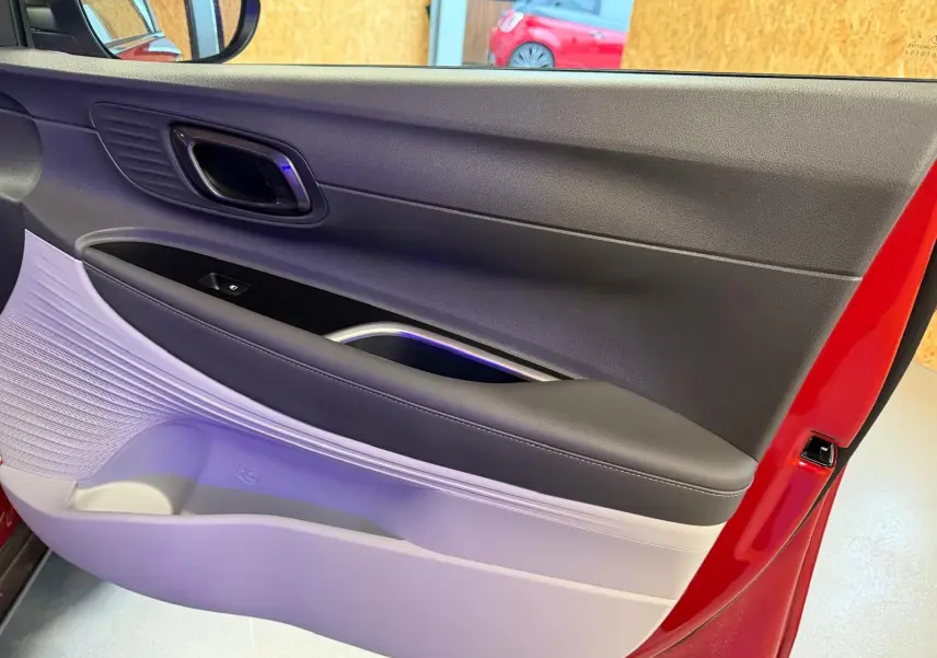 Vue rapprochée de la porte avant gauche rouge de la Hyundai BAYON 2025 avec intérieur bi-ton noir et gris clair.