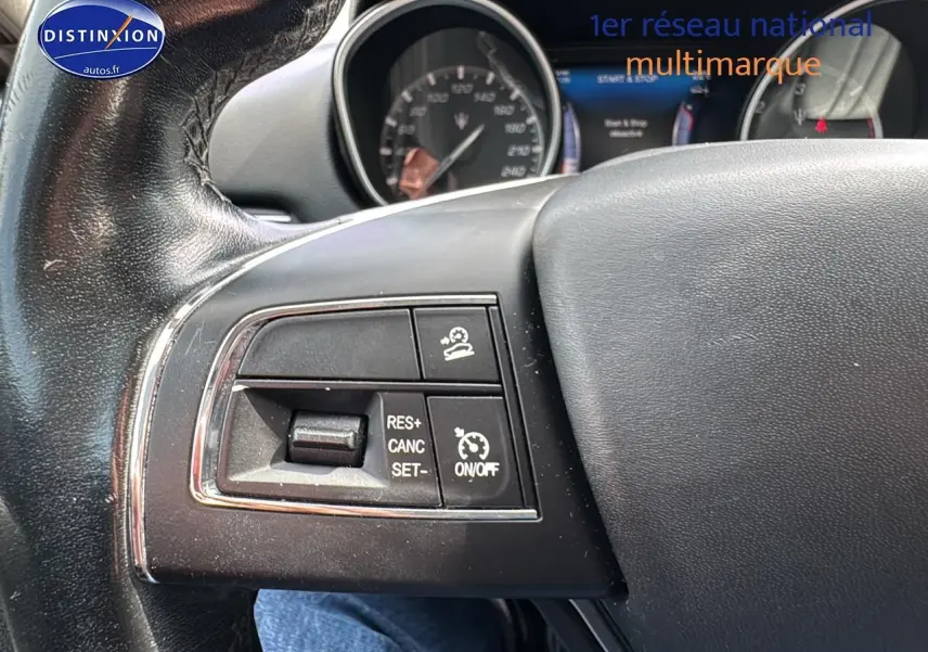 Gros plan sur les commandes de régulateur de vitesse au volant cuir noir d’un Maserati Levante gris.