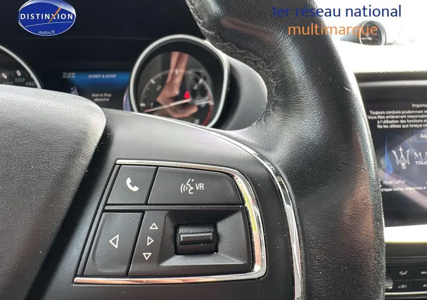 Gros plan sur les commandes au volant cuir noir du Maserati Levante gris, avec écran tactile visible en arrière-plan.