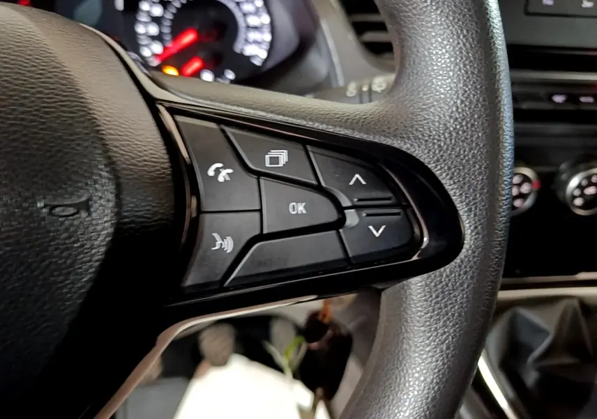 Gros plan sur les commandes multifonctions noires du volant côté droit du Renault Kangoo blanc, tableau de bord flou en arrière-plan.