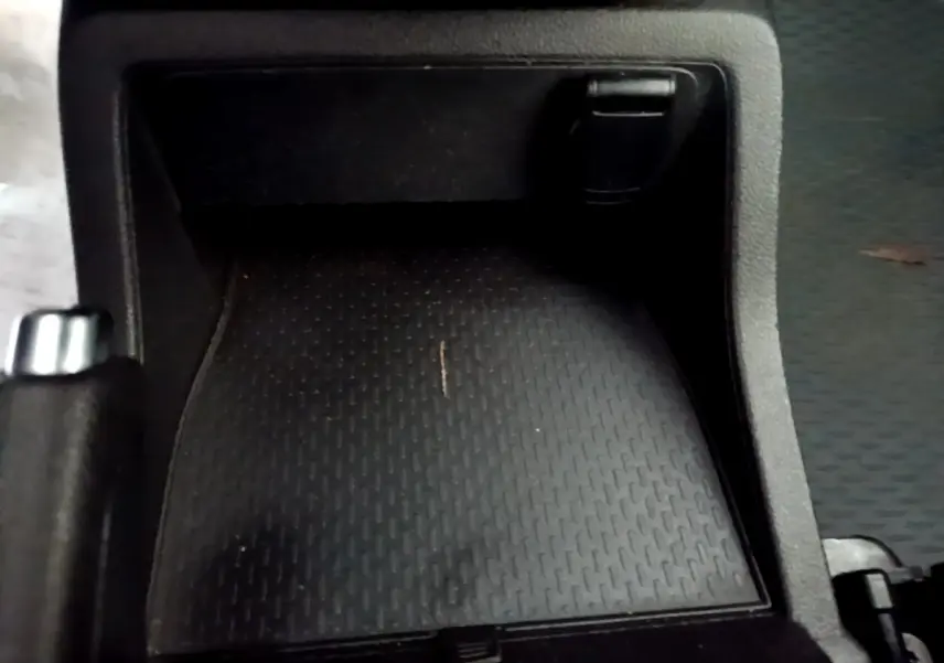 Gros plan sur le rangement central noir du Renault Kangoo blanc, version Equilibre Blue dCi 95, avec levier de frein à main visible.