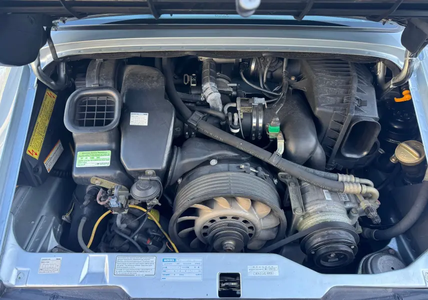 Vue plongeante sur le moteur essence d'une Porsche 911 Carrera 2 gris polaire de 1996, capot ouvert.