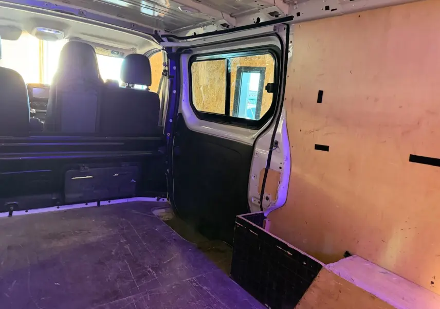 Vue intérieure arrière droite du Renault Trafic blanc avec habillage bois sur les parois et sièges avant visibles.