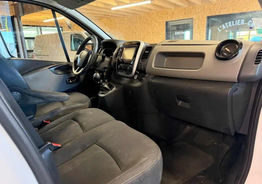 Vue intérieure côté conducteur du Renault Trafic Fourgon blanc, mettant en valeur le tableau de bord et les sièges en tissu noir.