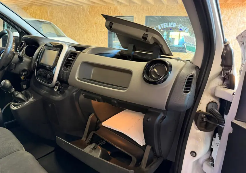 Vue intérieure côté passager du Renault Trafic Fourgon blanc 2017, tableau de bord avec boîte à gants ouverte et habillage bois visible.