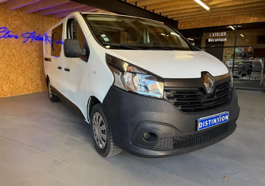 Renault Trafic Fourgon blanc en 3/4 avant droit, avec pare-chocs noir et intérieur habillage bois visible.
