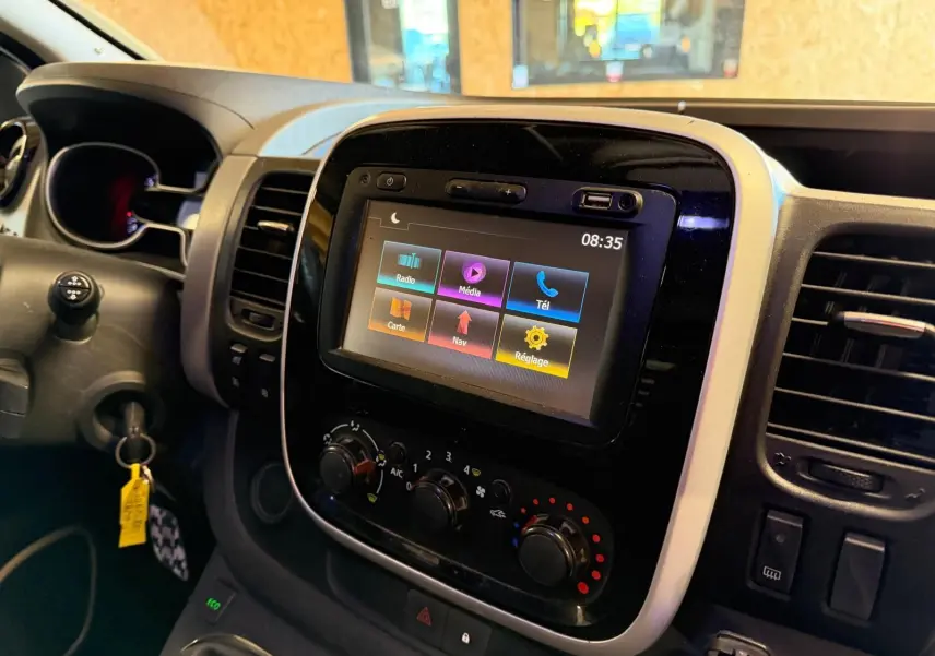 Vue rapprochée du tableau de bord du Renault Trafic Fourgon blanc, avec écran tactile et commandes de climatisation.