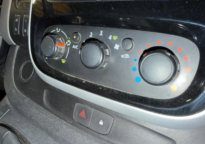 Gros plan sur les commandes de climatisation et ventilation du Renault Trafic Fourgon blanc, avec boutons rotatifs noirs.