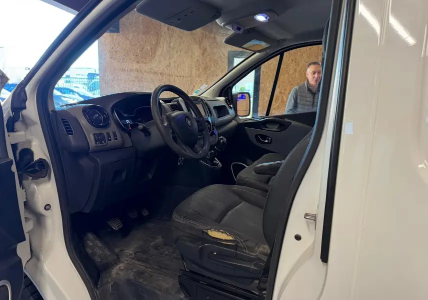 Vue intérieure côté conducteur du Renault Trafic blanc, montrant le tableau de bord et siège usé avec volant et levier de vitesse.