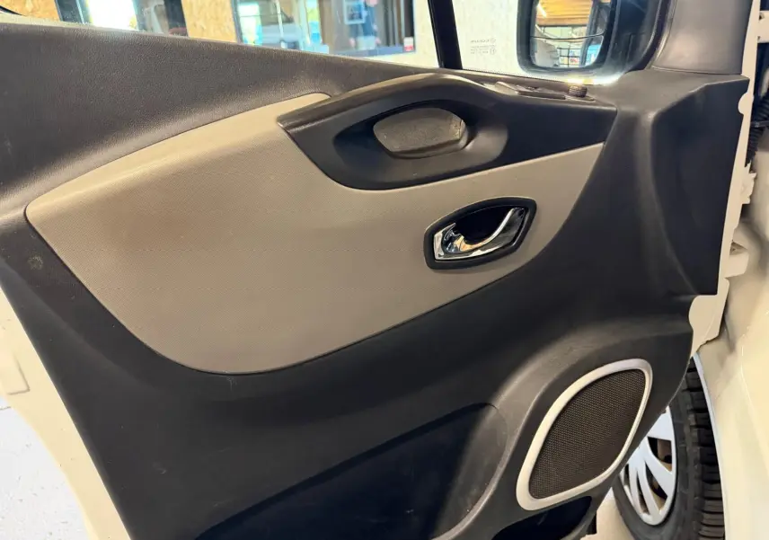 Vue intérieure côté gauche de la porte avant d’un Renault Trafic blanc, avec habillage bois et haut-parleur intégré.