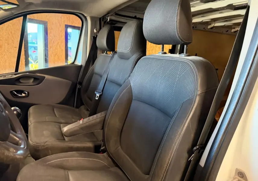 Vue intérieure côté gauche du Renault Trafic Fourgon 2017, sièges avant en tissu noir avec habillage bois visible en arrière-plan.