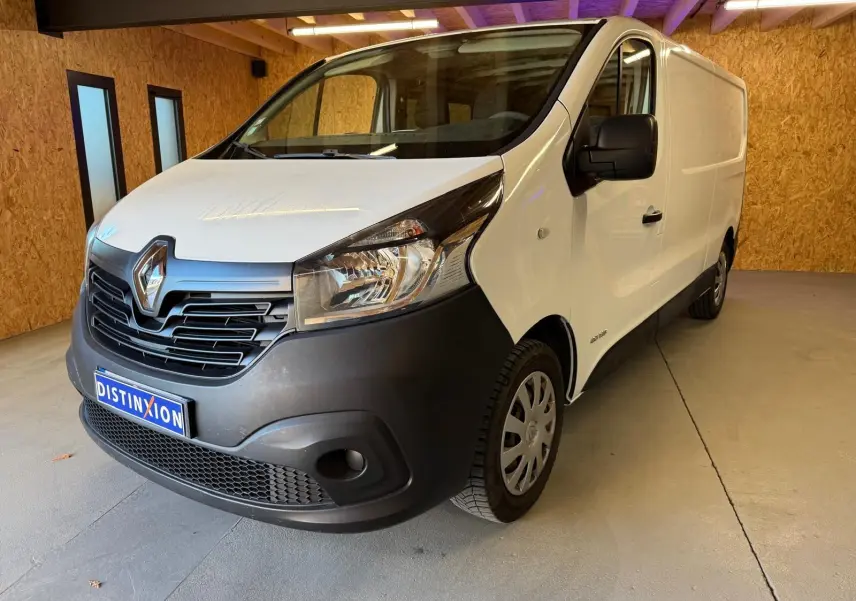 Renault Trafic Fourgon blanc en 3/4 avant droit, avec pare-chocs noir et intérieur habillage bois visible.