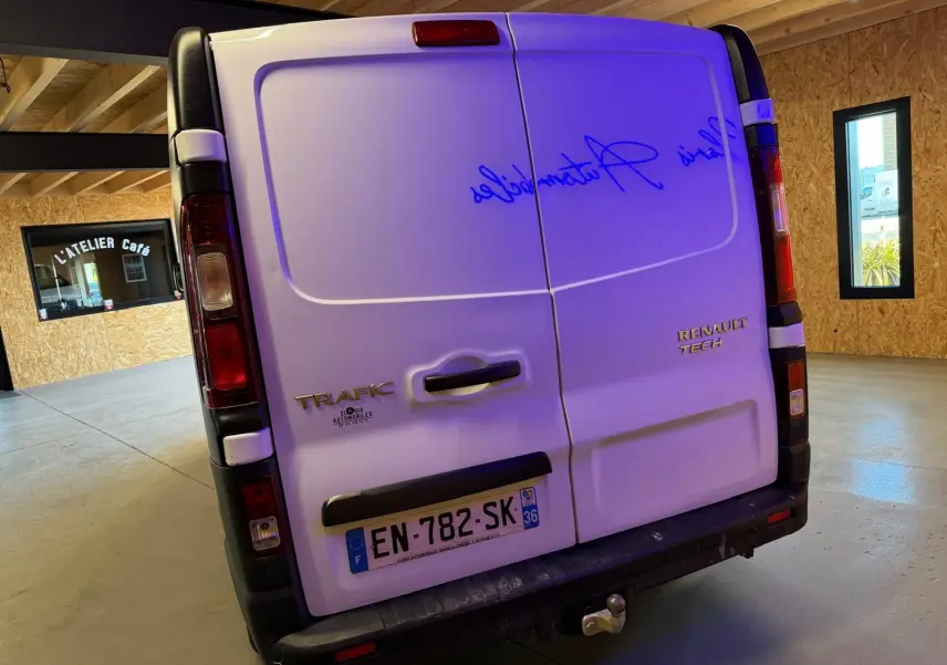 Vue arrière d'un Renault Trafic fourgon blanc de 2017 avec attelage, dans un garage au sol béton.