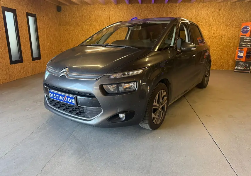 Vue 3/4 avant droit d'une Citroën C4 Picasso gris métallisé dans un showroom avec éclairage intérieur.