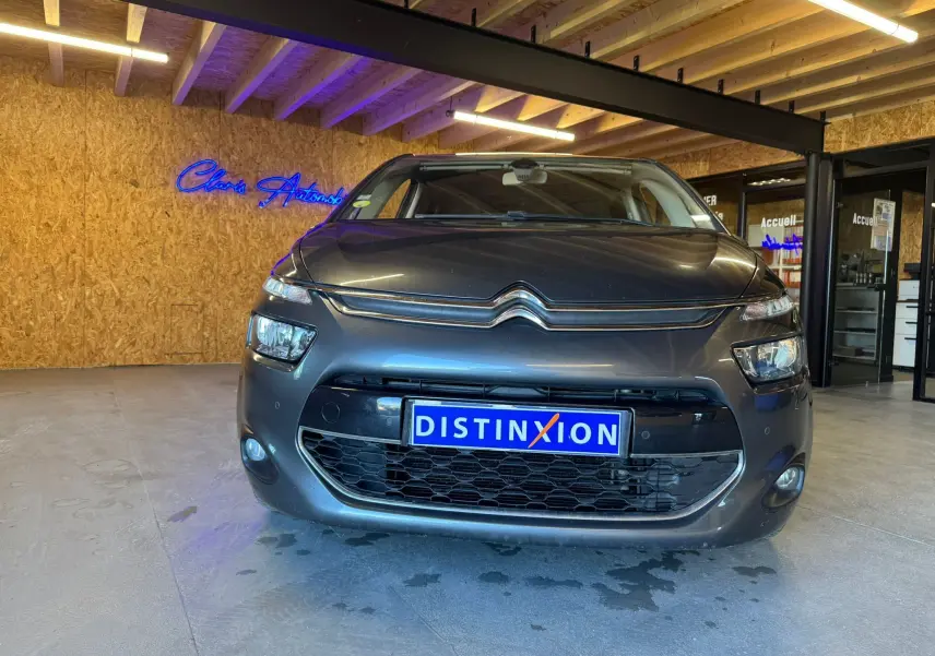 Vue avant d'une Citroën C4 Picasso gris métallisé, avec calandre et phares distinctifs, en intérieur showroom.