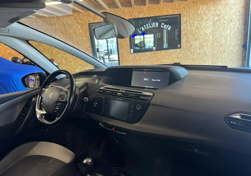 Vue intérieure côté conducteur du Citroën C4 Picasso gris, volant cuir multifonctions et écran central allumé.