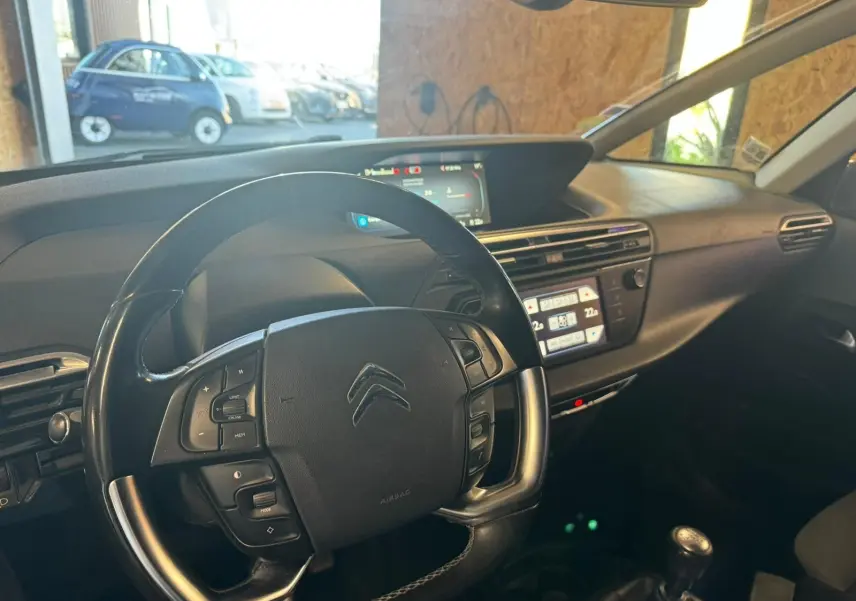 Vue intérieure centrée sur le volant cuir multifonctions et tableau de bord numérique de la Citroën C4 Picasso gris.