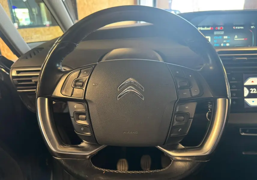 Vue rapprochée du volant cuir multifonctions noir de la Citroën C4 Picasso 2016 avec tableau de bord numérique en arrière-plan.