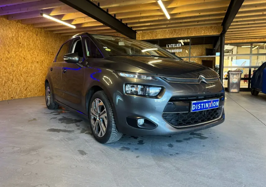 Citroën C4 Picasso gris vue 3/4 avant droit en intérieur avec jantes alu et éclairage LED distinctif.