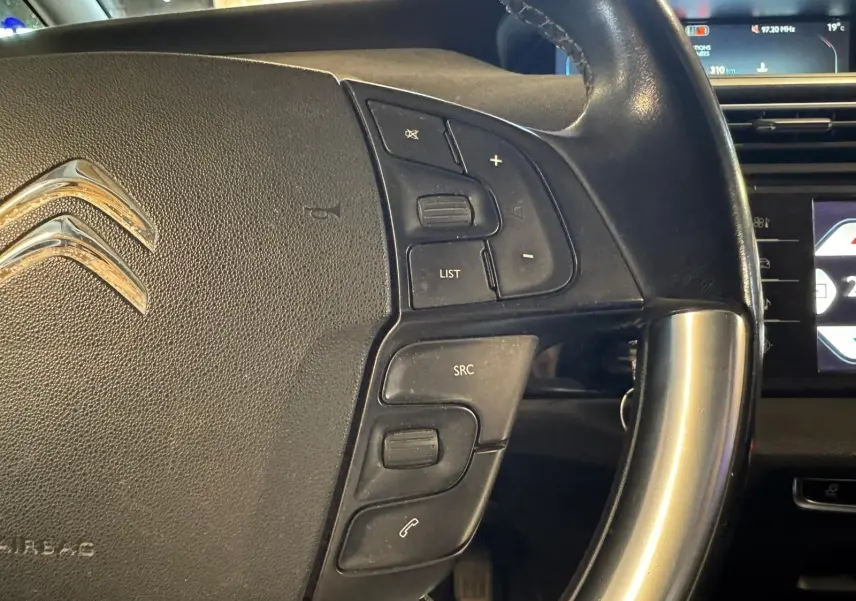 Gros plan sur le volant cuir multifonctions noir d'une Citroën C4 Picasso 2016 avec commandes audio et écran de bord en arrière-plan.