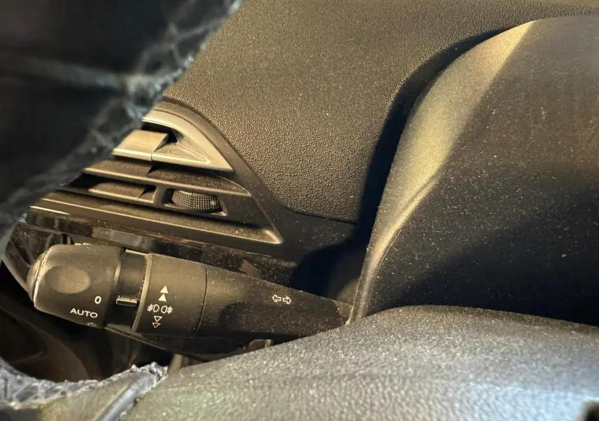 Gros plan sur la commande des feux et clignotants à gauche du volant noir dans l'habitacle du Citroën C4 Picasso gris.