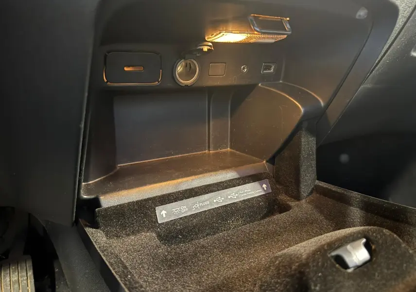 Vue rapprochée de la boîte à gants noire du Citroën C4 Picasso 2016 avec prise allume-cigare et éclairage intérieur.