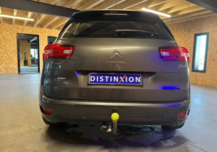 Vue arrière d'une Citroën C4 Picasso gris métallisé avec attelage et feux rouges dans un garage lumineux.