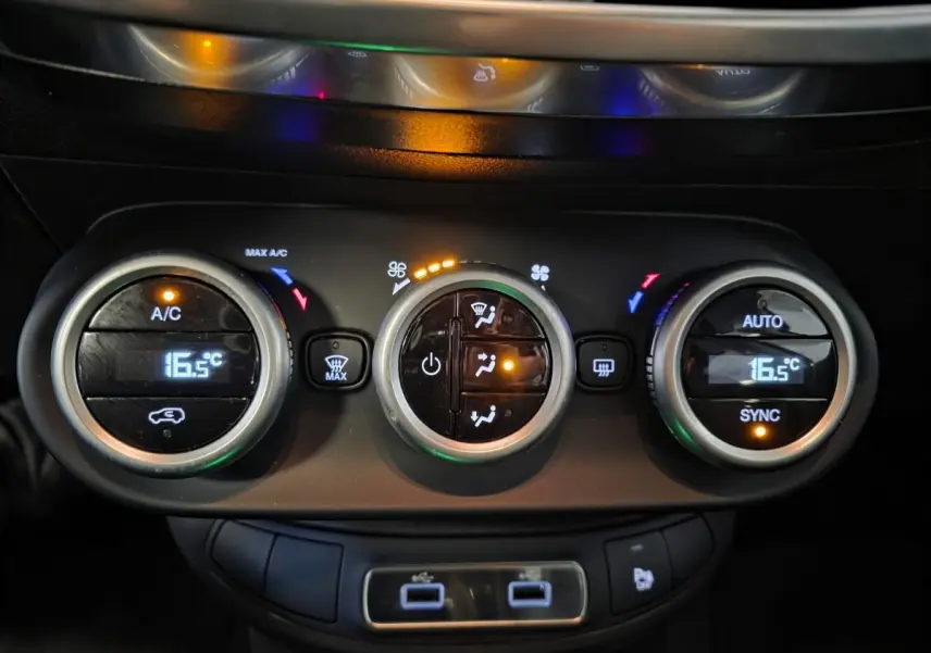 Gros plan sur la commande de climatisation bi-zone avec affichage digital à 16,5°C et ports USB du Fiat 500X rouge 2024.