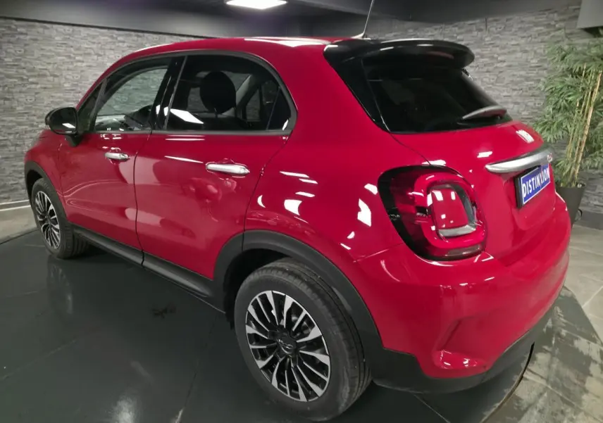 Vue 3/4 arrière droite d'un Fiat 500X rouge avec jantes alliage 17 pouces et vitres surteintées dans un intérieur gris.