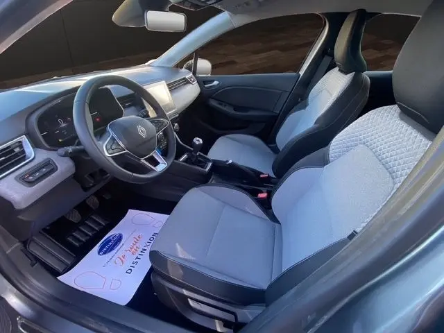 Vue intérieure côté conducteur de la Renault Clio gris foncé 2025, avec sièges tissu gris clair et tableau de bord moderne.