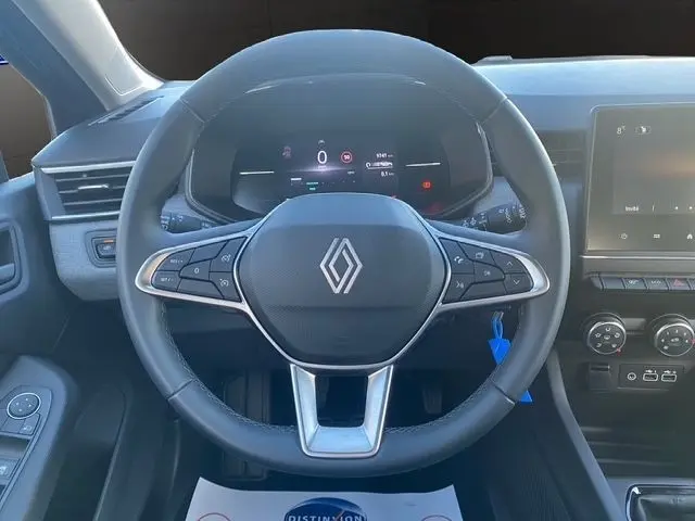 Vue intérieure centrée sur le volant cuir synthétique de la Renault Clio gris foncé, avec tableau de bord numérique et écran tactile visible à droite.