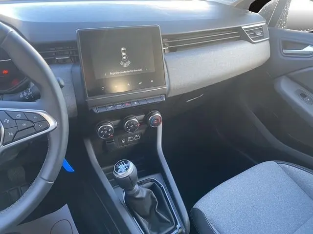 Intérieur de la Renault Clio Evolution Blue dCi 100 2025, vue côté passager, tableau de bord gris et console centrale avec écran tactile.