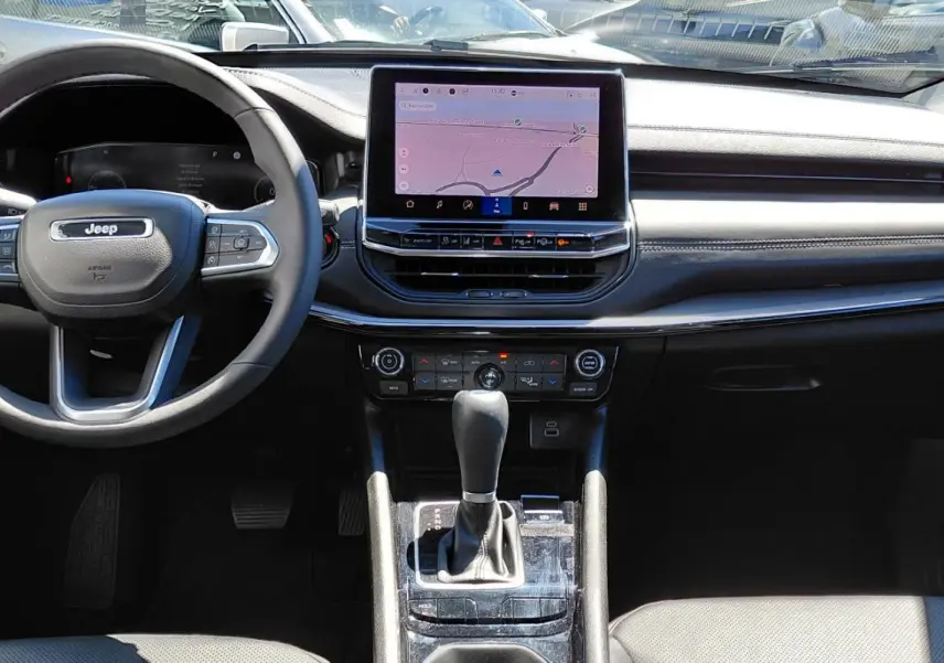 Vue frontale de l’intérieur noir du Jeep Compass 2025 avec volant multifonction et écran tactile central.
