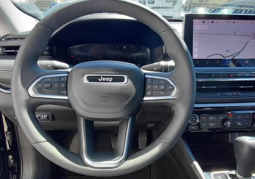 Vue intérieure centrée sur le volant Jeep noir et l'écran tactile du tableau de bord du Compass 2025.