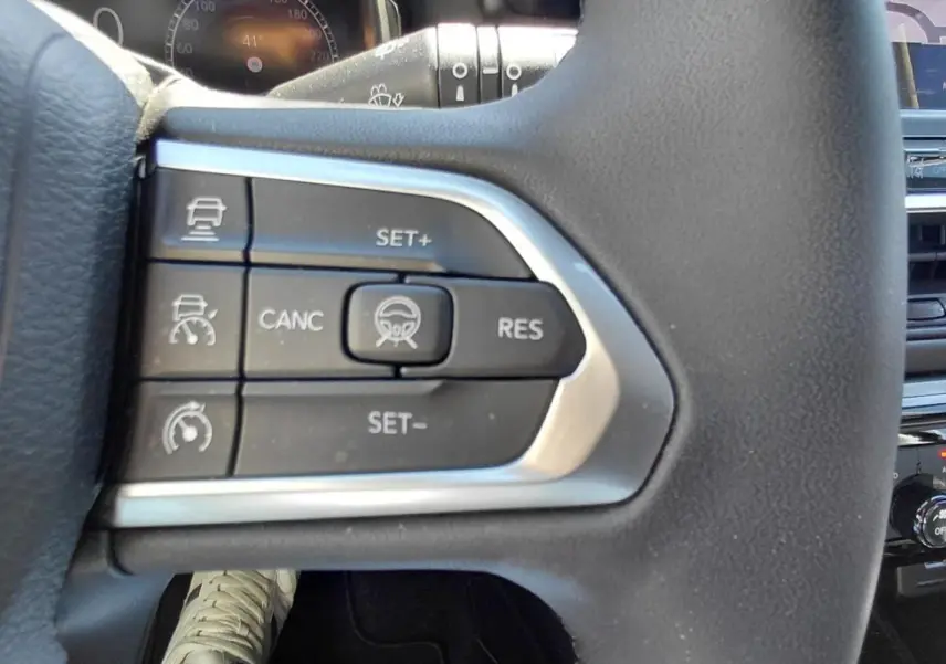 Gros plan sur les commandes du volant noir du Jeep Compass 2025, avec tableau de bord et console centrale en arrière-plan.
