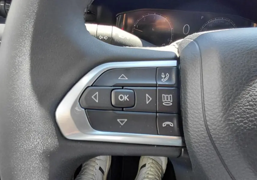 Gros plan sur les commandes multifonctions à gauche du volant noir du Jeep Compass 2025, avec tableau de bord en arrière-plan.